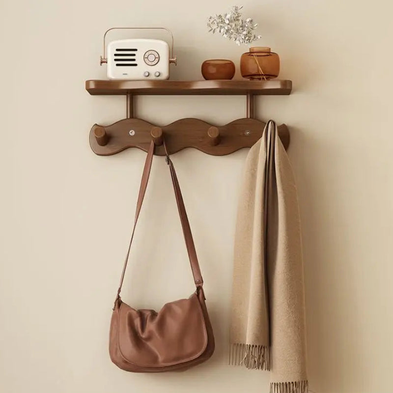 Wall-mounted wooden shelf with hooks holding a handbag and scarf against a beige wall.