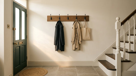 Oak wall-mounted coat rack with coats and a tote bag in a British hallway, between the front door and the staircase