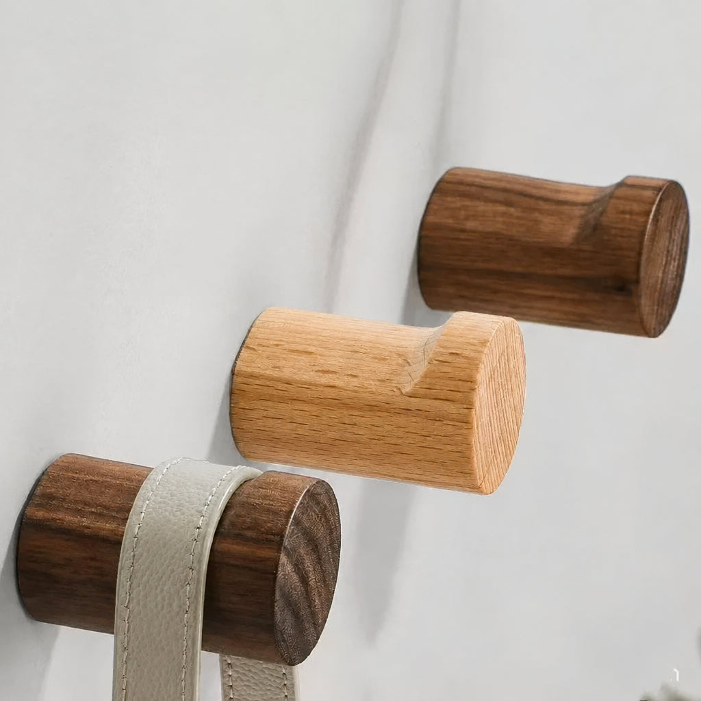 Three natural wooden wall hooks in different wood tones mounted on a white wall, with one hook holding a light beige leather strap. Text at the top reads 'Natural Wooden Wall Hooks'.