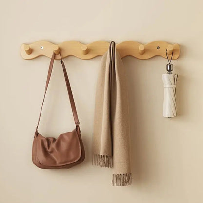 Wooden wall hook with a brown bag, beige scarf, and white umbrella on a beige wall.