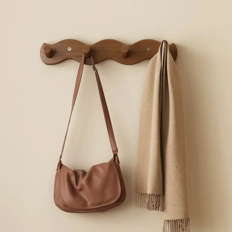 A wall-mounted wooden coat rack with four hooks in a warm brown finish, shown hanging a brown shoulder bag and a beige scarf against a cream wall. Chinese text at the bottom indicates the rack is small, tea-colored, with four hooks and dimensions of 33*5cm.