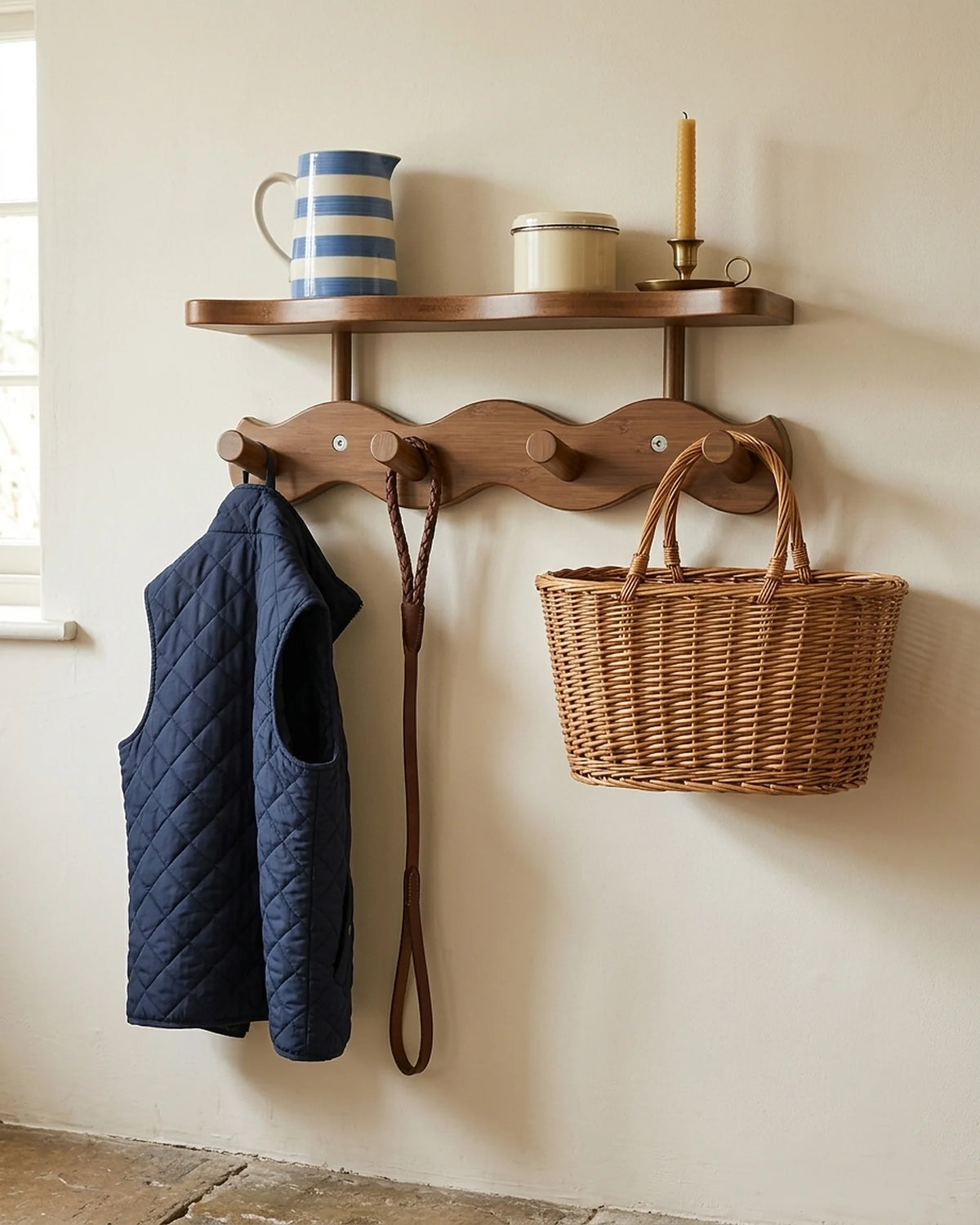 Walnut-finish bamboo wavy coat rack with a shelf holding a navy gilet, a dog lead and a wicker basket in a cottage boot room