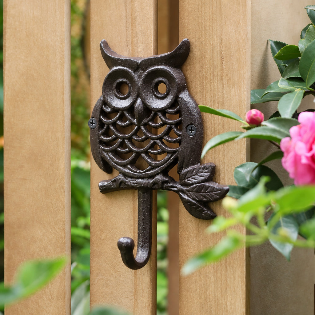 Round cast iron owl wall hook perched on a leafy branch, mounted on a wooden garden fence