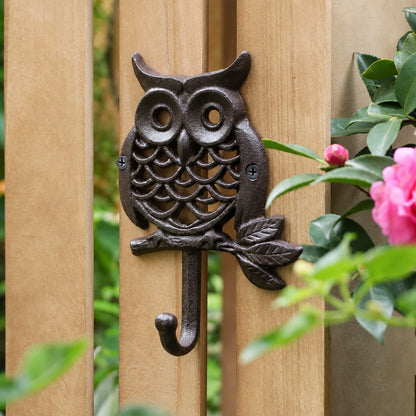 Round cast iron owl wall hook perched on a leafy branch, mounted on a wooden garden fence