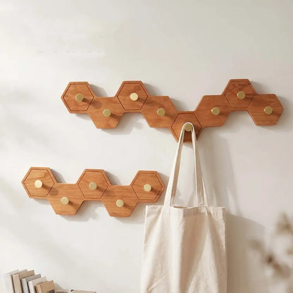 Honeycomb wall hooks of linked wooden hexagons in a cherry finish with brass pegs, holding a tote bag