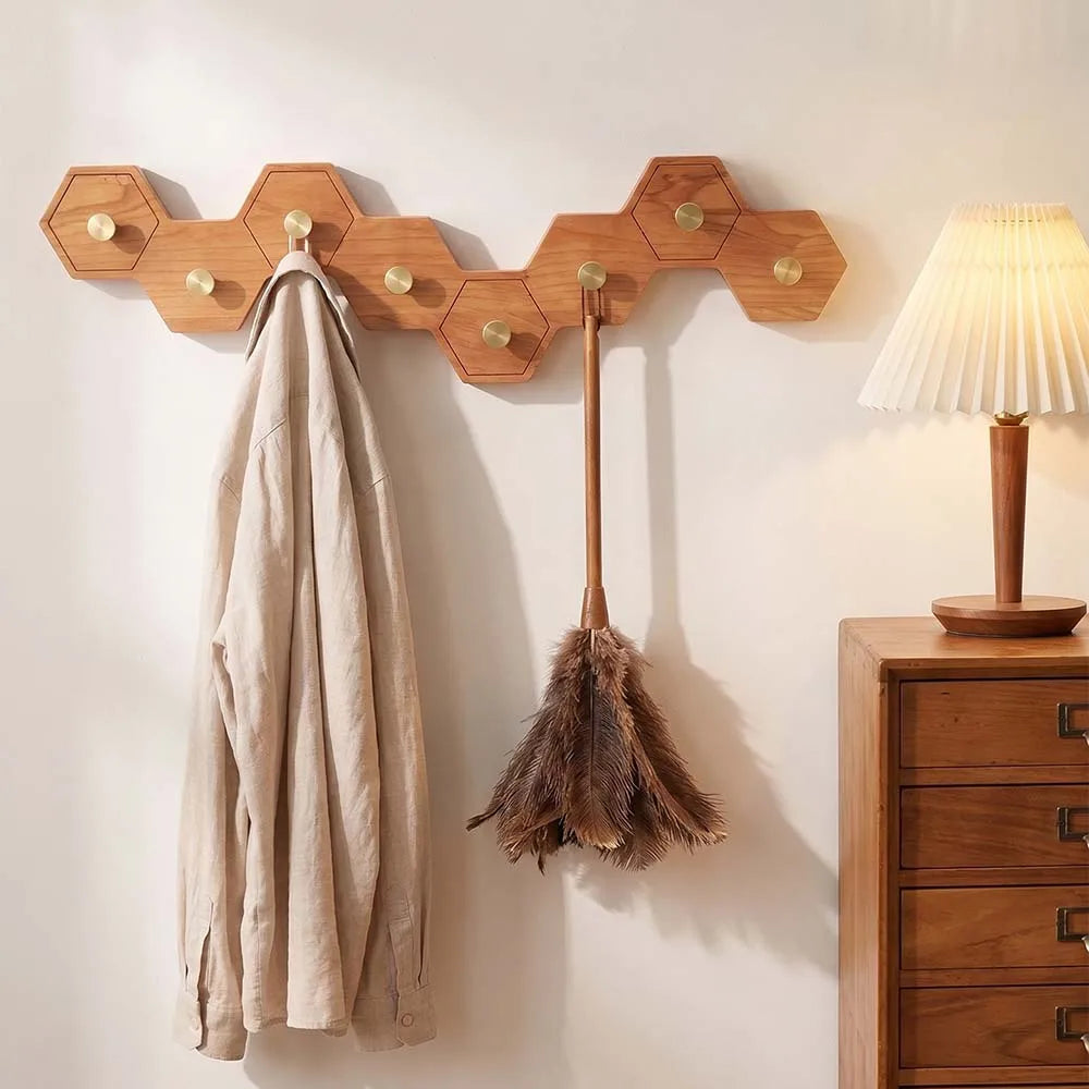 Honeycomb wooden wall hooks holding a coat and a feather duster beside a chest of drawers