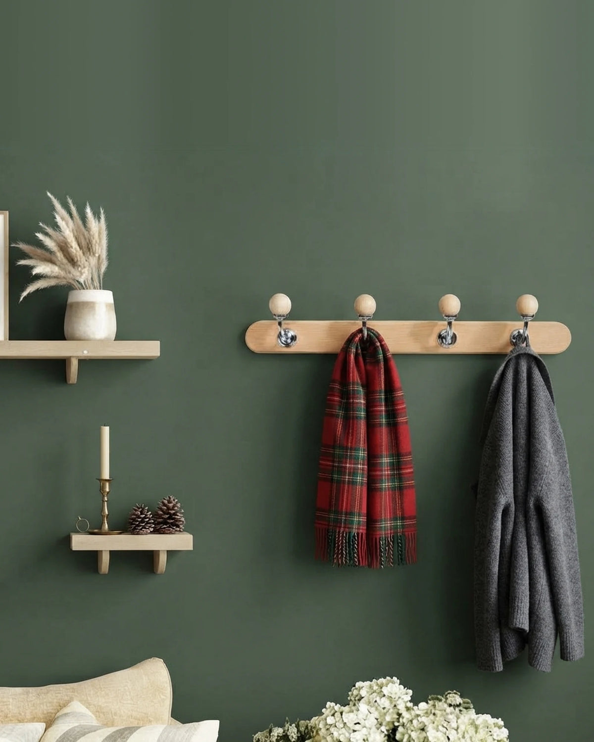 Natural wood coat rack with chrome ball-top hooks on a moss green wall, holding a tartan scarf and a charcoal knitted cardigan