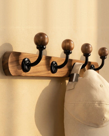 Close-up of the walnut-colour coat rack with black ball-top hooks, holding a cream cotton cap
